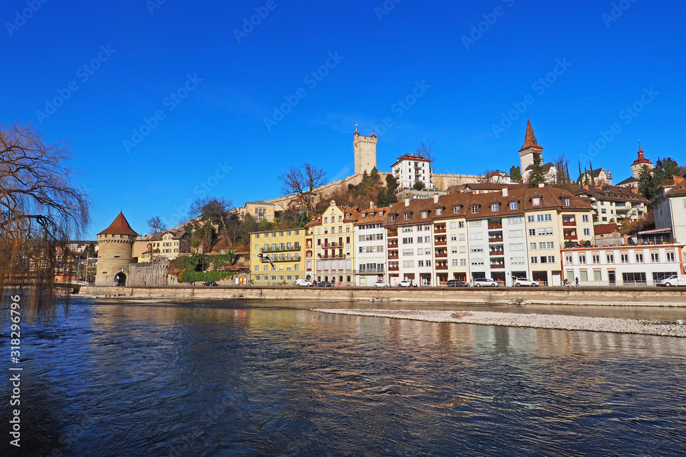 Lucerne along Reuss River with medieval city wall and towers against deep blue sky.