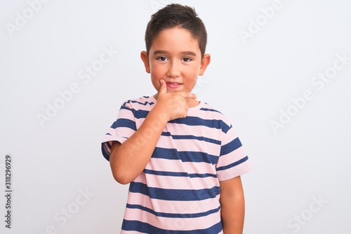 Beautiful kid boy wearing casual striped t-shirt standing over isolated white background looking confident at the camera with smile with crossed arms and hand raised on chin. Thinking positive.