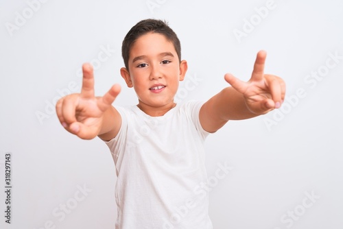 Beautiful kid boy wearing casual t-shirt standing over isolated white background smiling looking to the camera showing fingers doing victory sign. Number two.