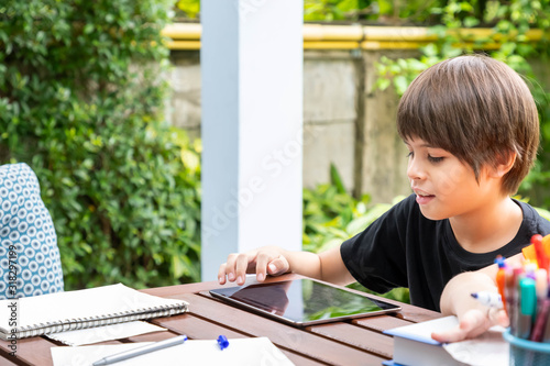 Cute boy using tablet while doing homework in garden at home