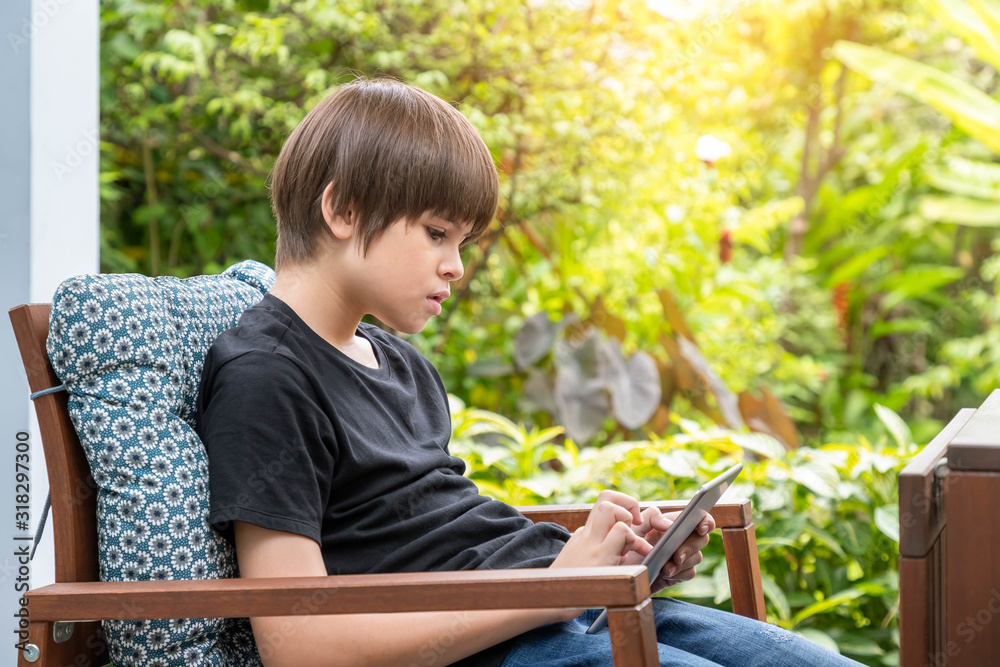Young cute Caucasian boy using digital tablet sitting on couch in garden at home Young cute Caucasian boy using digital tablet sitting on couch in garden at home