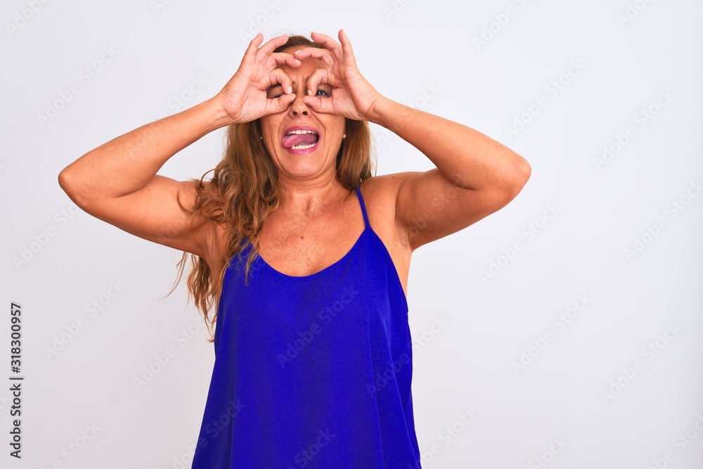 Middle age mature woman standing over white isolated background doing ok gesture like binoculars sticking tongue out, eyes looking through fingers. Crazy expression. Middle age mature woman standing over white isolated background doing ok gesture like binoculars sticking tongue out, eyes looking through fingers. Crazy expression.