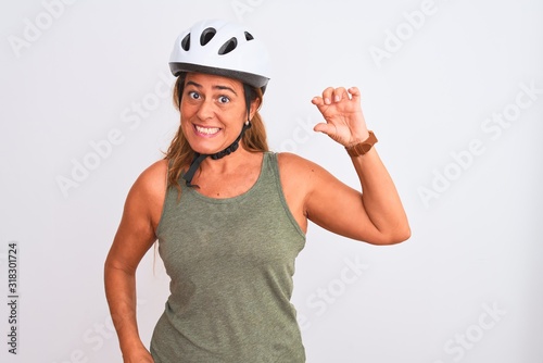 Middle age mature cyclist woman wearing safety helmet over isolated background smiling and confident gesturing with hand doing small size sign with fingers looking and the camera. Measure concept.