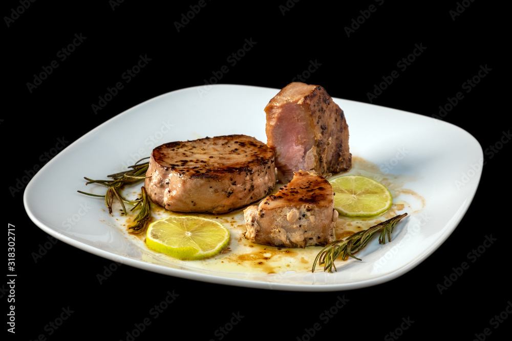 Freshly cooked grilled tuna steak with rosemary, lime, lemon on white plate. Seared tuna fish, roasted. Top view from above horizontal, close up, closeup