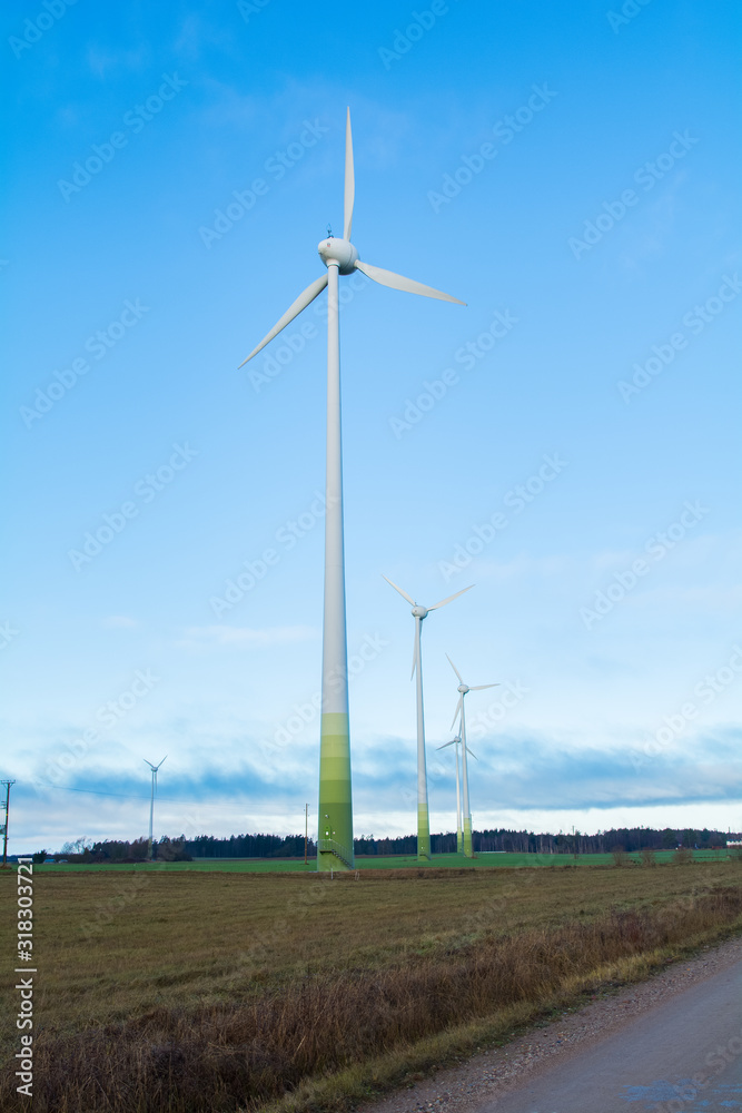 Wind electricity generator park, visible green farming fields, trees, grass and blue skies with clouds