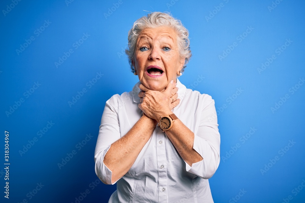 Senior beautiful woman wearing elegant shirt standing over isolated blue background shouting and suffocate because painful strangle. Health problem. Asphyxiate and suicide concept. Senior beautiful woman wearing elegant shirt standing over isolated blue background shouting and suffocate because painful strangle. Health problem. Asphyxiate and suicide concept.