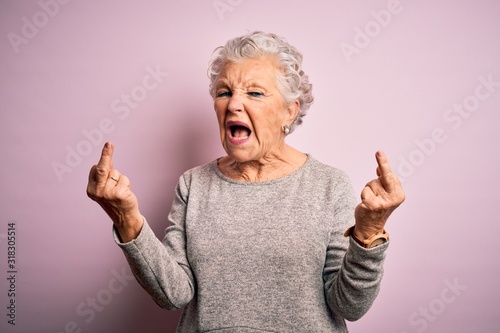 Senior beautiful woman wearing casual t-shirt standing over isolated pink background Showing middle finger doing fuck you bad expression, provocation and rude attitude. Screaming excited