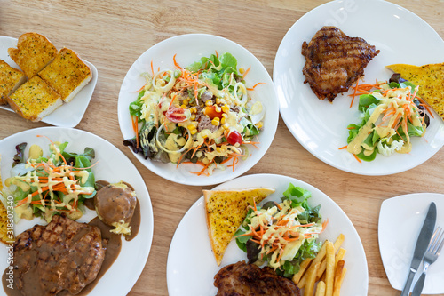 Close up knife and fork cutting grilled chicken steak set in white dish on wooden table background.Chicken grill, mashed potato, bread and salad.Restaurant menu.