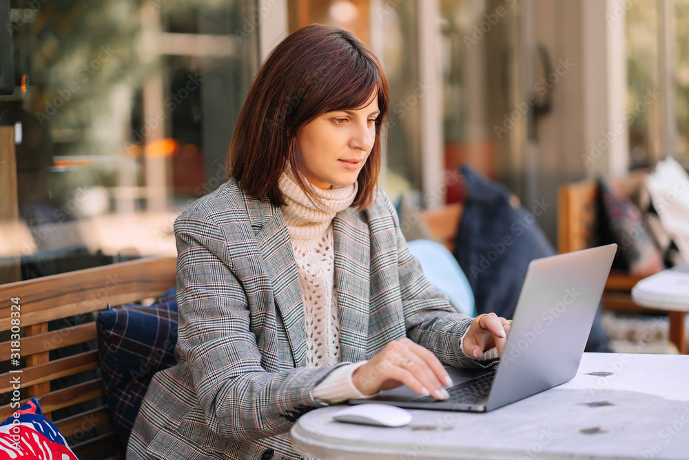 Young woman in warm sweater and blazer working on net-book in cafe on the terrace. Autumn morning. Street style. Young woman in warm sweater and blazer working on net-book in cafe on the terrace. Autumn morning. Street style.