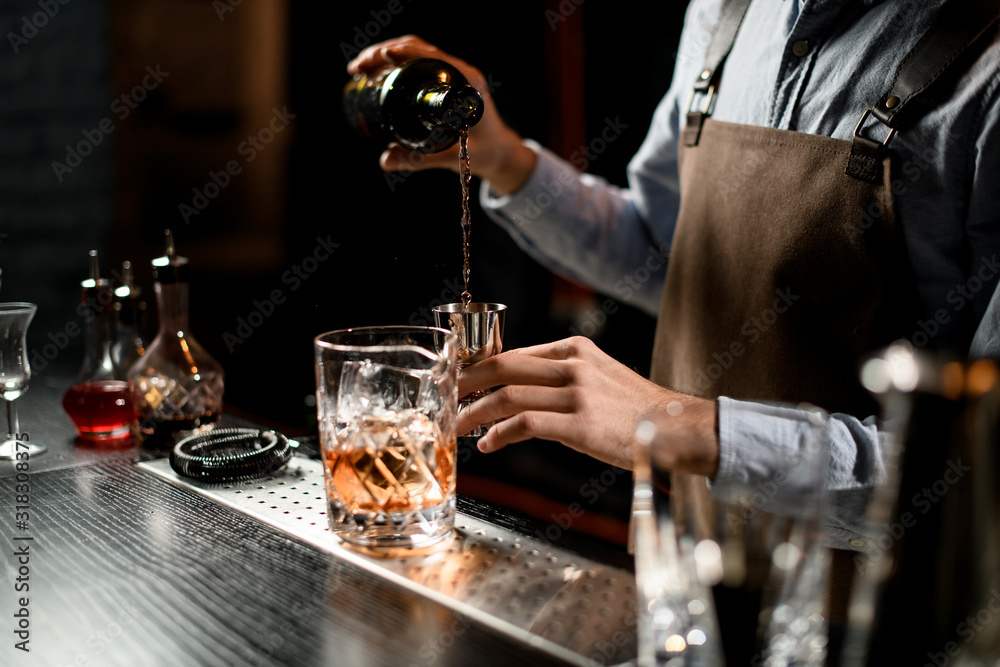 Bartender pouring a alcoholic drink from the bottle to a steel jigger