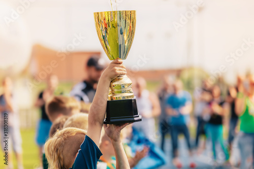 Happy kids in school sports team rising golden cup. Boys winning sports championship. Child holding big golden trophy photo