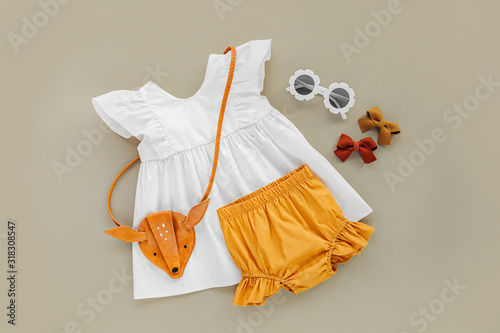 Wallpaper Mural White dress,  orange shorts with kids handbag and sunglasses. Set of  baby clothes and accessories for spring or summer on beige background. Fashion childs outfit. Flat lay, top view Torontodigital.ca