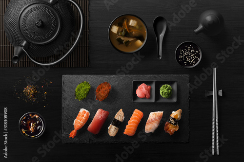 Sushi rolls, sashimi set, miso soup and teapot, on dark wooden table, Japanese food, top view. photo