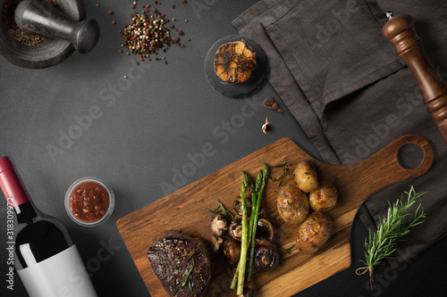 Steak with baked potatoes, asparagus, on wooden board, with wine and spices, top view with copy space