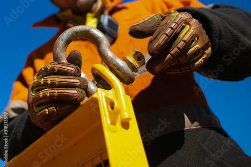 Close up rigger high risk worker wearing safety heavy duty glove, safety helmet fastening pin into D- shape shackle industry crane lifting lug gate prior lift at construction site Perth city photo