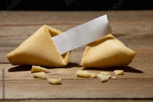 Close up of fortune cookie with blank paper inside and cookie crumbles on a bamboo board