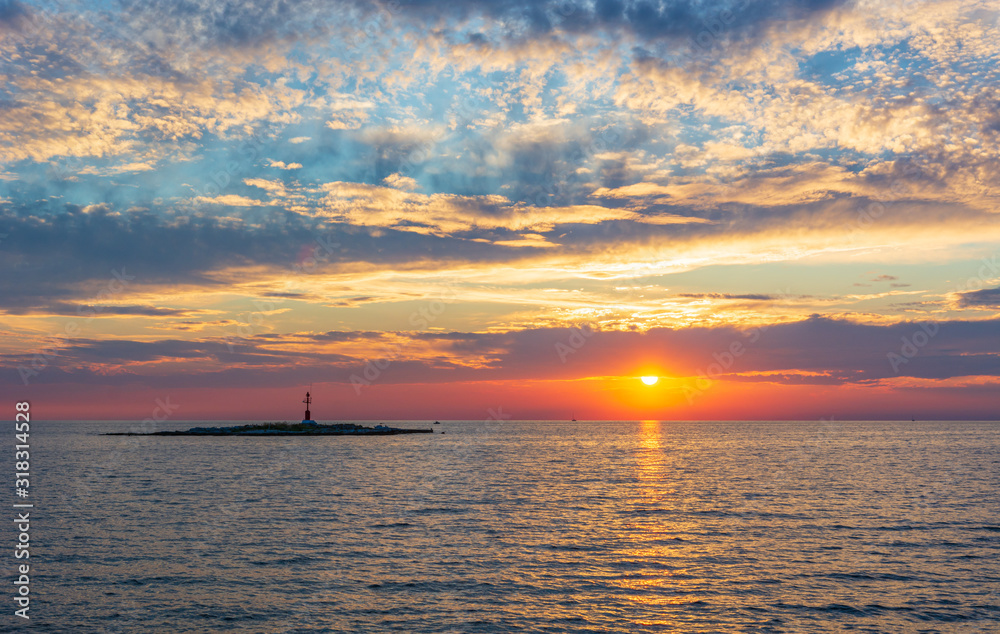 Ocean sunrise with small lighthouse on a island.