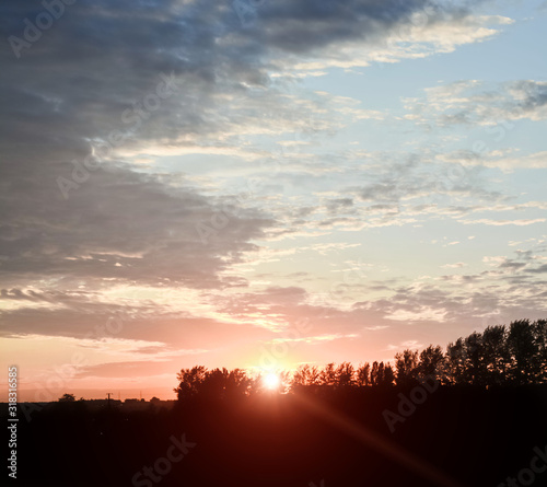 Early morning. Spring landscape in pink and blue.Pink and blue clouds at sunrise. Tender dawn paints over a dark forest silhouette.Beautiful natural scenery. Copy space.