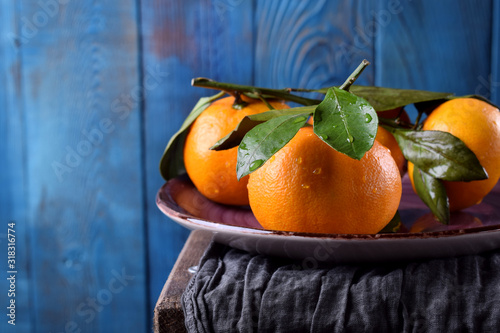 Mandarins with green leaves on the ceramic plate against the blue wooden background