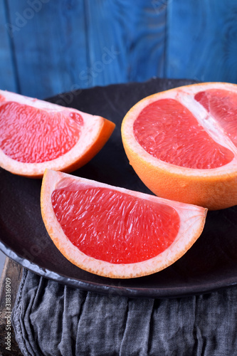 Slices of red grapefruit on the black plate against the blue wooden background