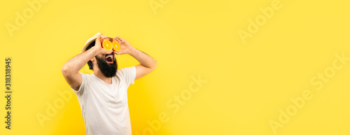 bearded hipster man holding lemon slices in front of eyes, over yellow background, panoramic mock-up with space for text