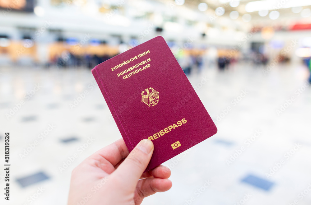 A hand holds a german passport in an airport terminal - obrazy, fototapety, plakaty 
