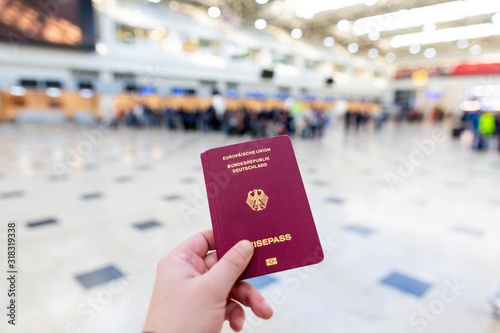 A hand holds a german passport in an airport terminal