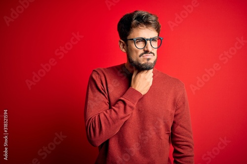 Young handsome man with beard wearing glasses and sweater standing over red background Touching painful neck, sore throat for flu, clod and infection