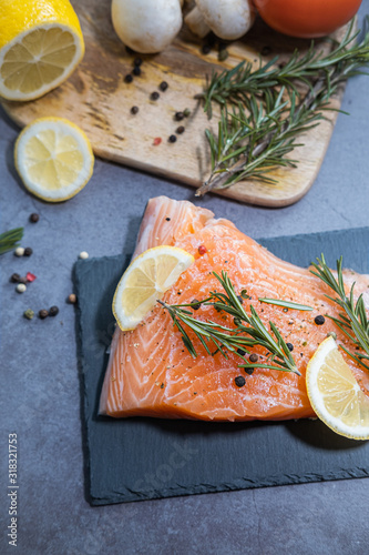 Fresh salmon on slate plate and ingredients on dark background.