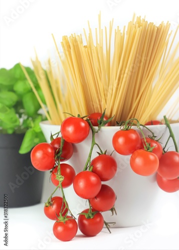 closeup of bowl with cherry tomatoes, spaghetti and basil jar on a white background