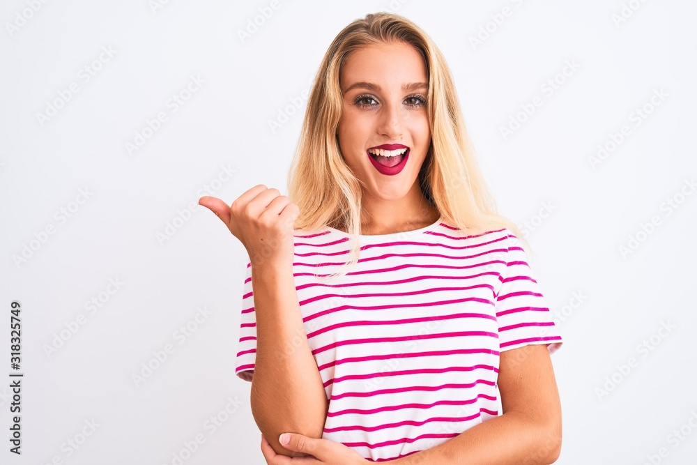 Young beautiful woman wearing pink striped t-shirt standing over isolated white background smiling with happy face looking and pointing to the side with thumb up. Young beautiful woman wearing pink striped t-shirt standing over isolated white background smiling with happy face looking and pointing to the side with thumb up.