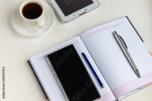 White office desk with necessary items on it. Diary with pen, Samsung phone. White cup of coffee. Top view with copy space,