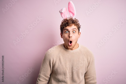 Young handsome blond man wearing easter rabbit ears over isolated pink background afraid and shocked with surprise expression, fear and excited face.