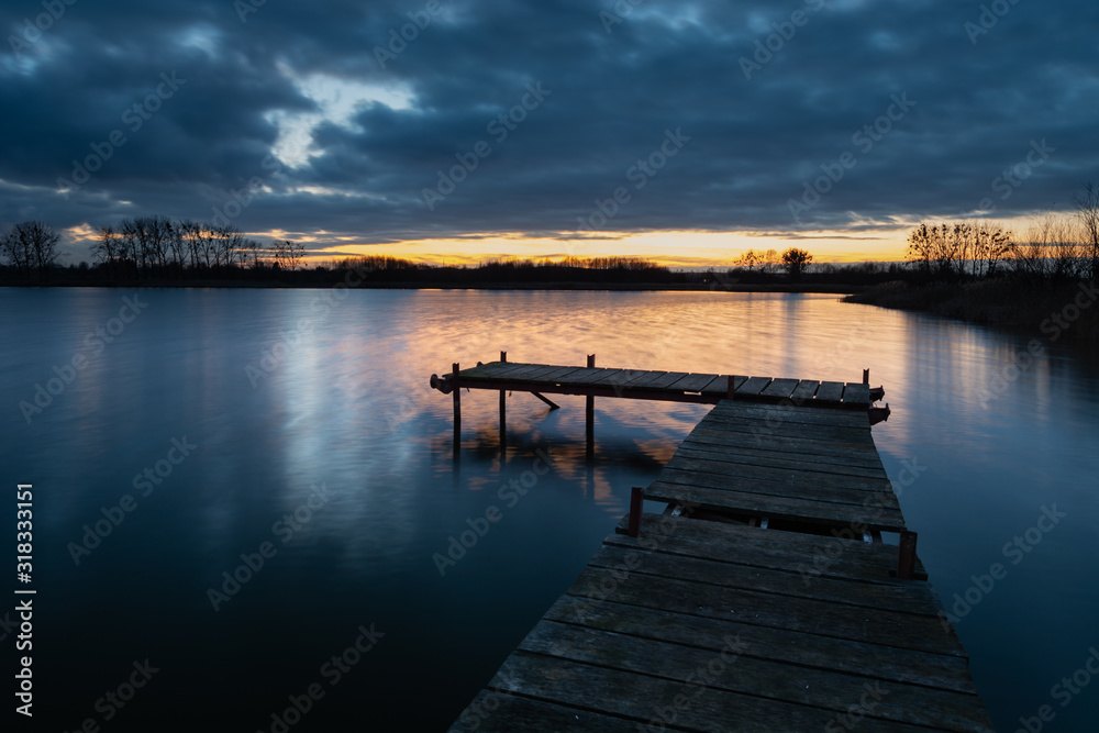 Wooden deck bridge and evening clouds after sunset over the water, view in december day