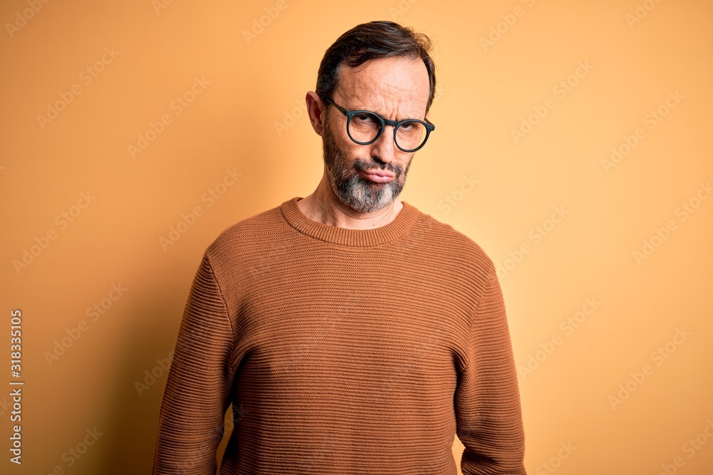 Fototapeta premium Middle age hoary man wearing brown sweater and glasses over isolated yellow background depressed and worry for distress, crying angry and afraid. Sad expression.