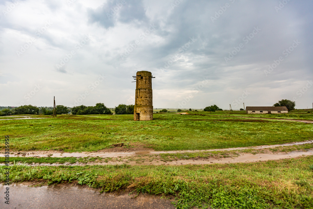 old brick tower standing on the outskirts of the village by a dirt road after rain