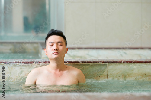 Young Asian Man relaxing with eyes closed enjoying hot tub in modern spa salon, horizontal shot