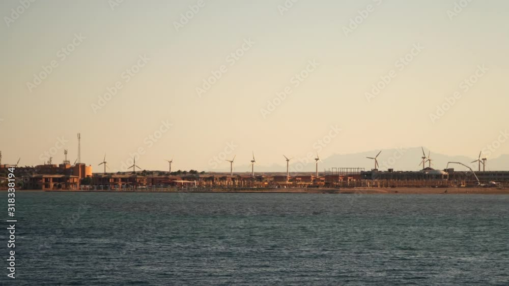 Wind turbines on the coast. View from the sea from the ship. Evening time Wind turbines on the coast. View from the sea from the ship. Evening time
