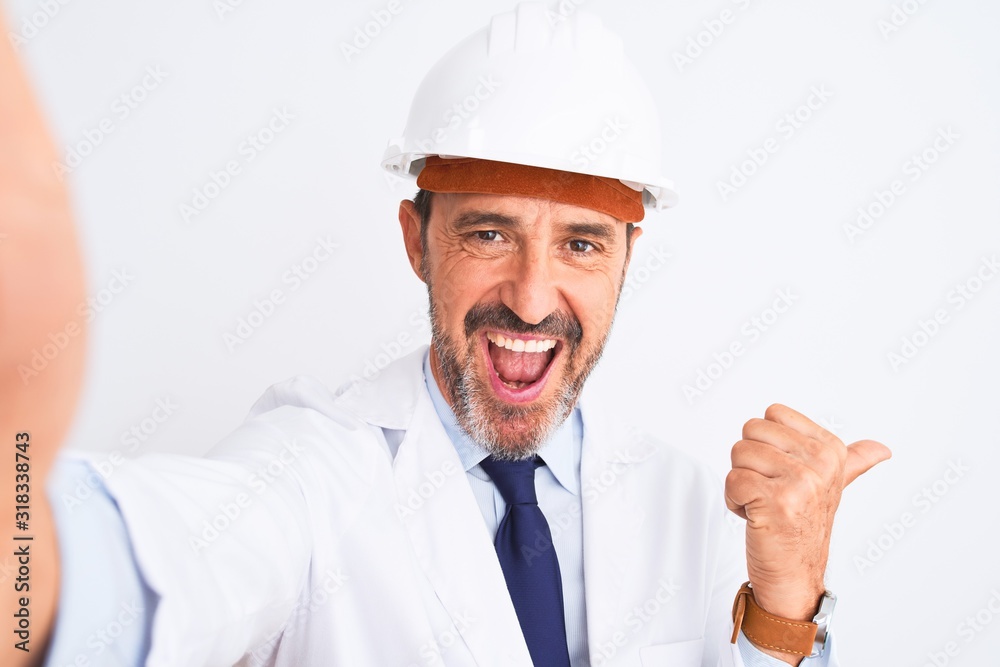 Middle age engineer man wearing helmet make selfie over isolated white background pointing and showing with thumb up to the side with happy face smiling Middle age engineer man wearing helmet make selfie over isolated white background pointing and showing with thumb up to the side with happy face smiling