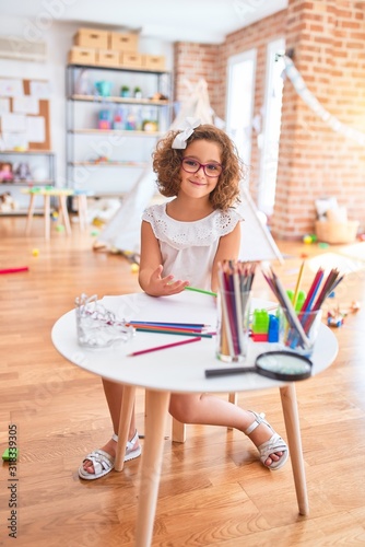 Beautiful toddler wearing glasses sitting drawing using paper and pencils at kindergarten