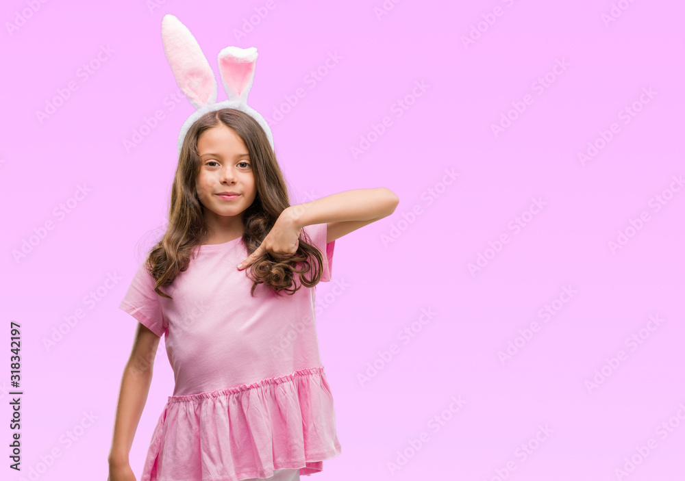 Brunette hispanic girl wearing easter rabbit ears with surprise face pointing finger to himself Brunette hispanic girl wearing easter rabbit ears with surprise face pointing finger to himself