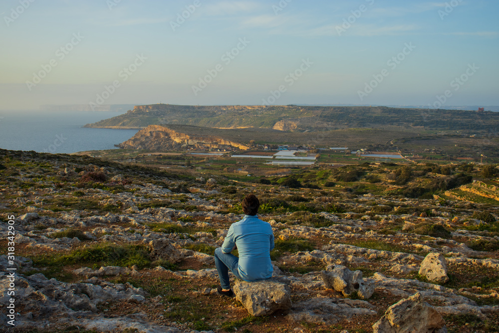 Fototapeta premium Man sitting and watching a beautiful scenery at Malta
