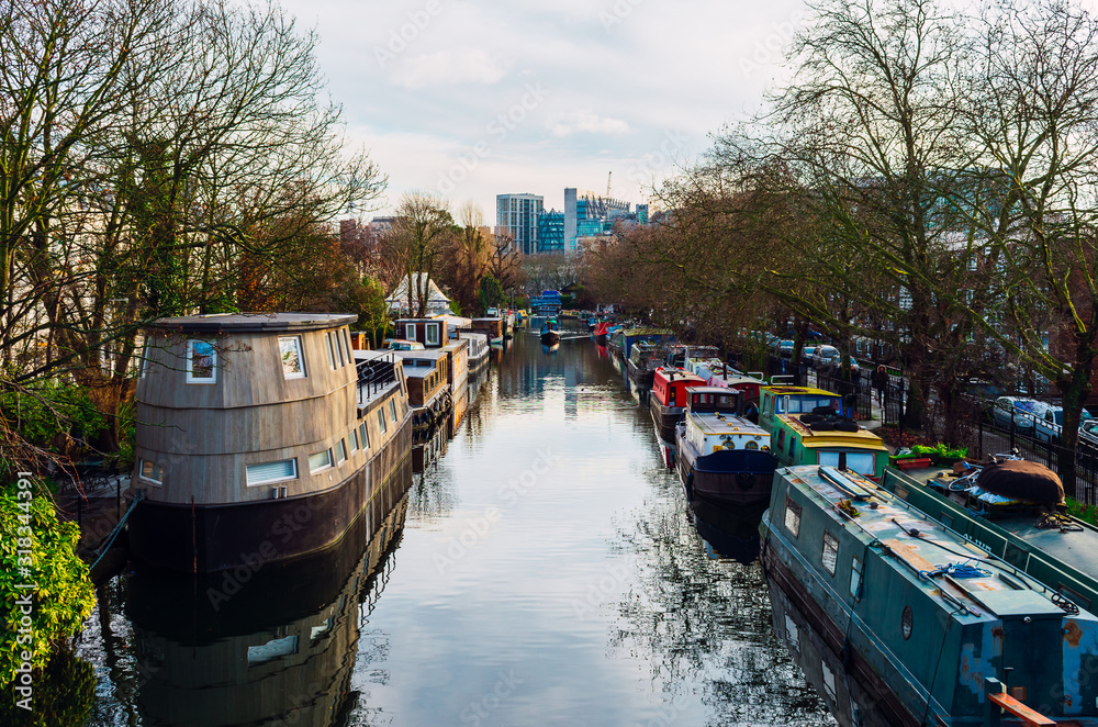 Naklejka premium Boat traveling between parked houseboats through a canal in Little Venice district, London