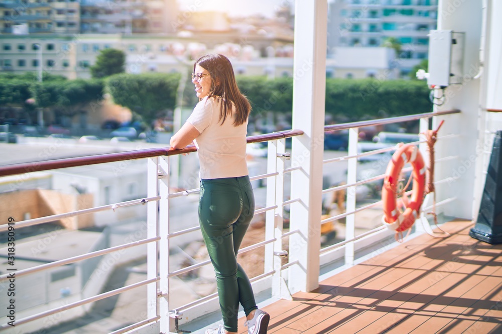 Young beautiful woman on vacation smiling happy and confident. Standing on a deck of ship with smile on face doing a cruise