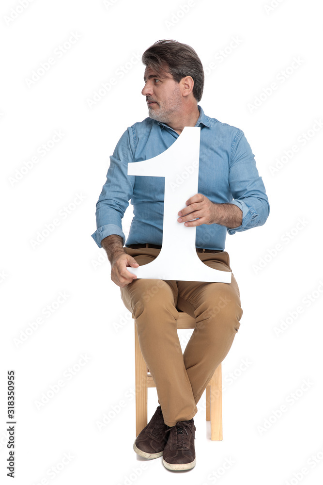 Confident casual man looking away while holding a number one Confident casual man looking away while holding a number one