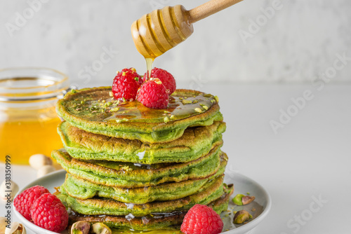 Matcha tea green pancakes. Pile of homemade pancakes with fresh raspberries, pistachios and flowing honey