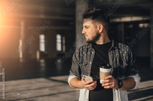 Young handsome man waitin for friend with cup of coffee and talking by phone photo