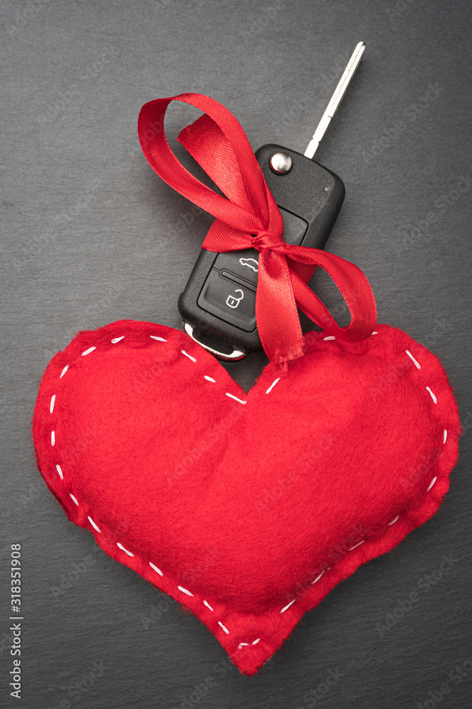 Car key with red bow and a heart on dark black slate plate background. Christmas or Valentine's Day gift or present abstract concept. Vertical orientation. Flat lay top view.