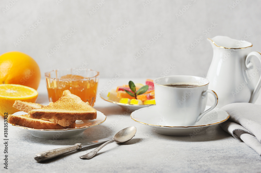 Coffee and toast with orange jam. The concept of an elegant breakfast setting. Oranges, cream, marmalade complete the composition. Light background. Close-up. Coffee and toast with orange jam. The concept of an elegant breakfast setting. Oranges, cream, marmalade complete the composition. Light background. Close-up.