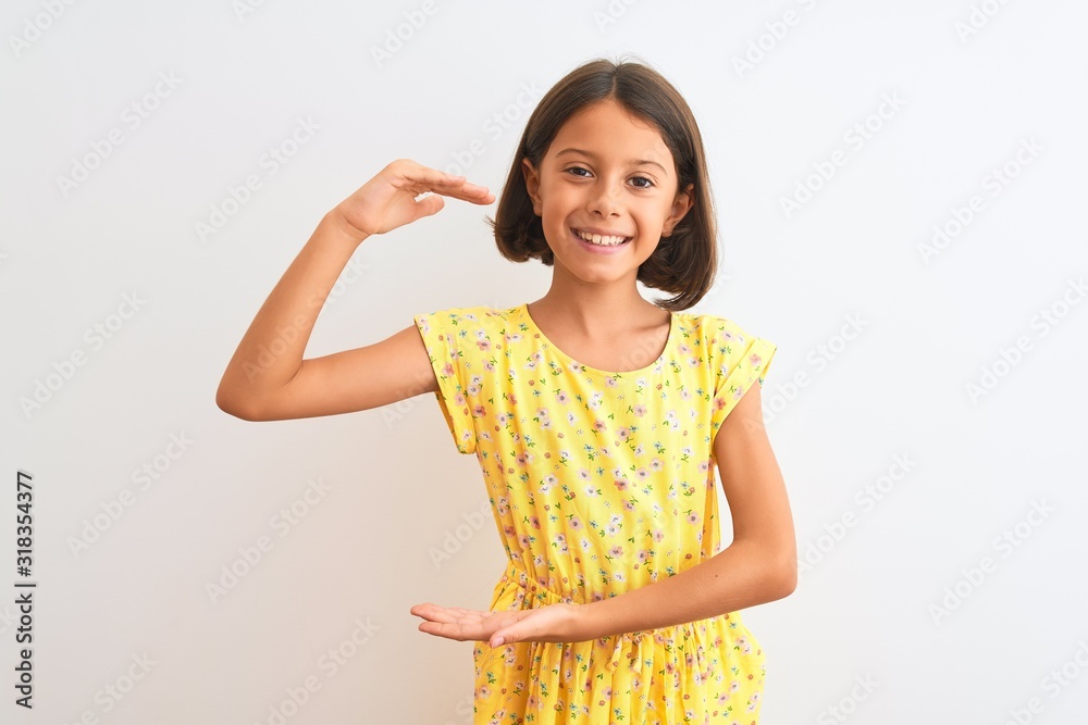 Young beautiful child girl wearing yellow floral dress standing over isolated white background gesturing with hands showing big and large size sign, measure symbol. Smiling looking at the camera Young beautiful child girl wearing yellow floral dress standing over isolated white background gesturing with hands showing big and large size sign, measure symbol. Smiling looking at the camera